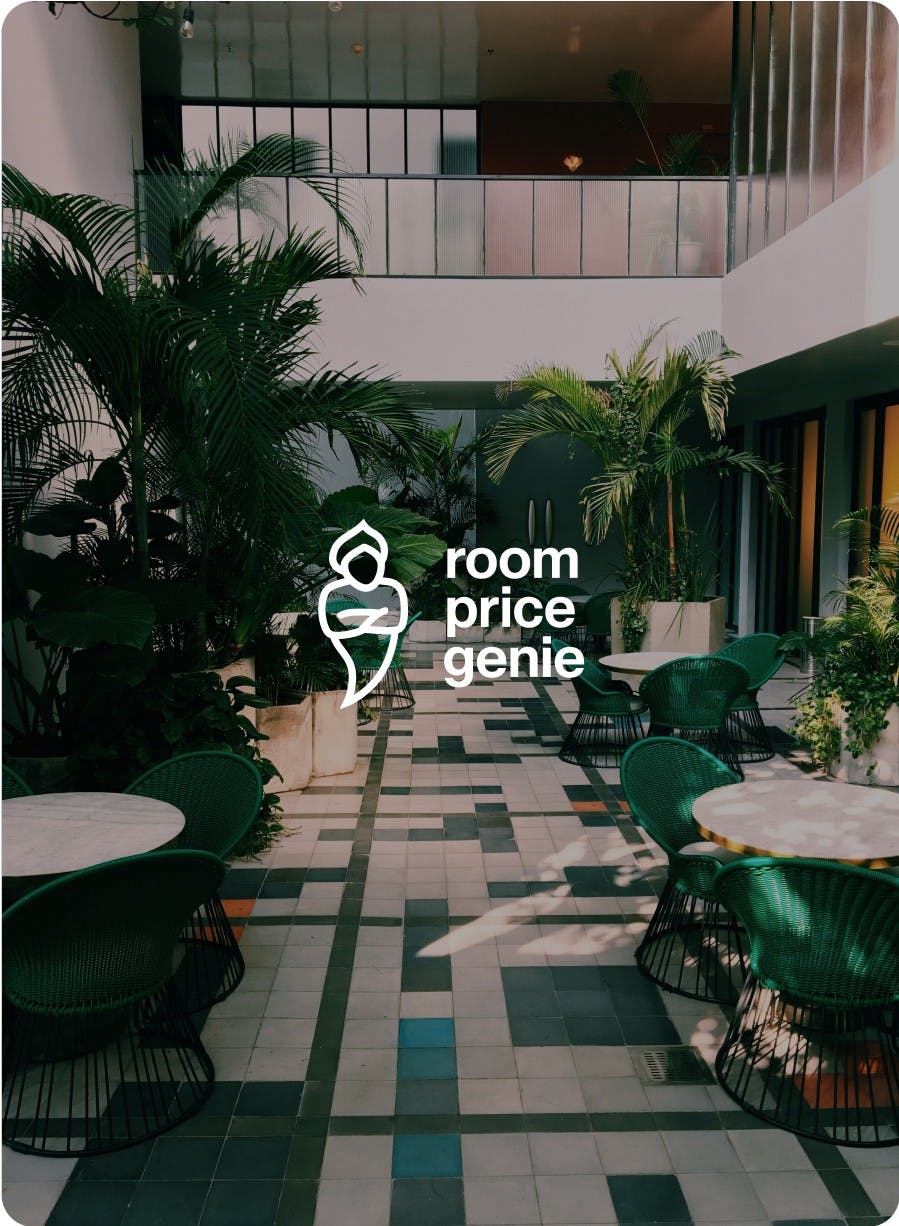 RoomPriceGenie Logo on top of an image showing an elegant hotel lobby filled with palmtrees and lounge furniture