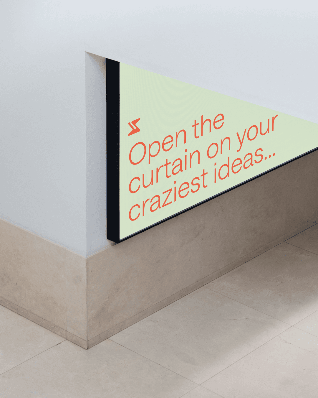 A corner of a room with light-colored walls and floor. A triangular wall panel features text in red: "Open the curtain on your craziest ideas..." with a small red arrow symbol above the text.