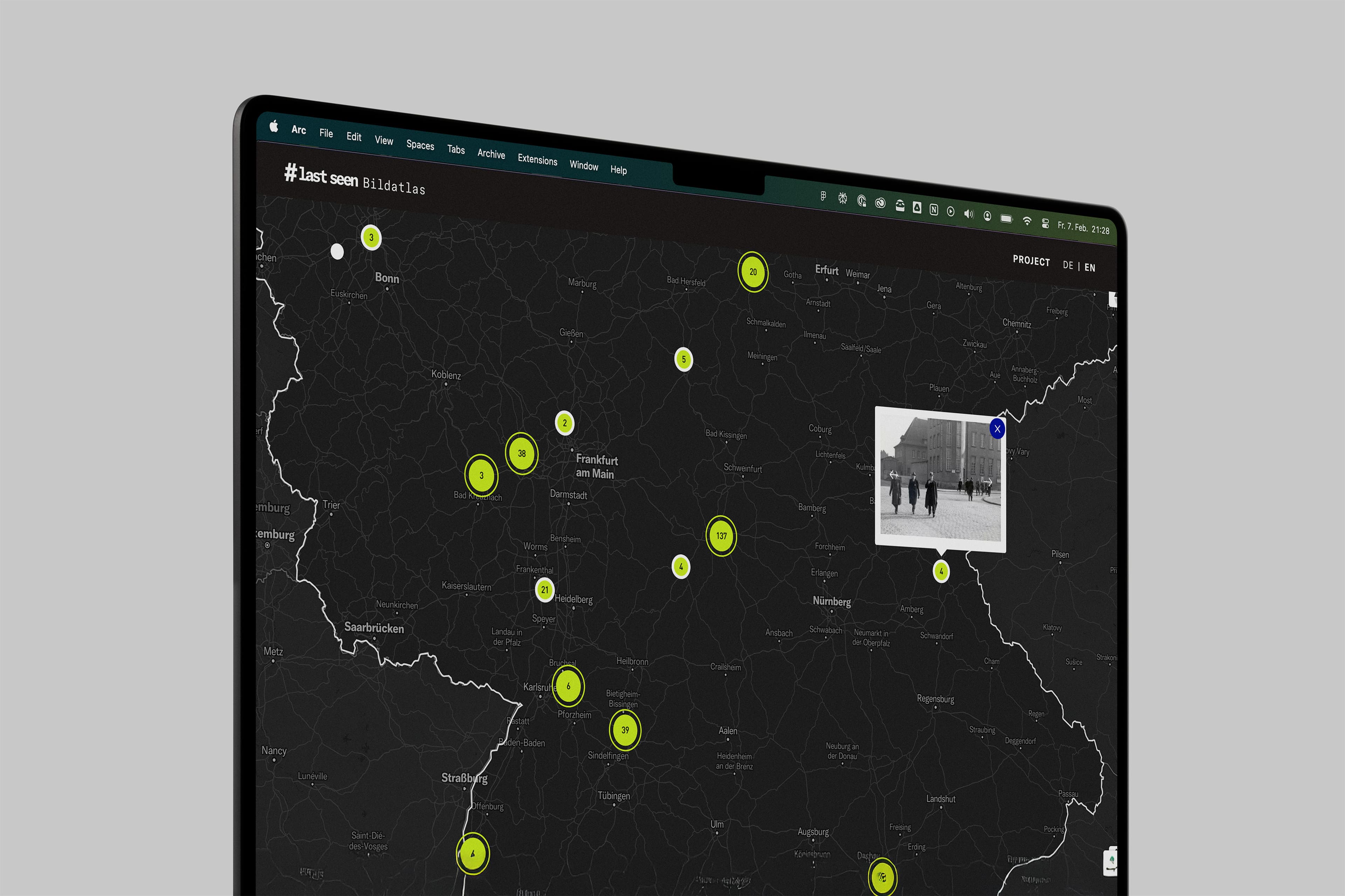 A computer screen displays a map with multiple bright green markers, indicating locations in a geographic area. A small black and white photo is shown near one marker. The interface includes various navigation and filter options.