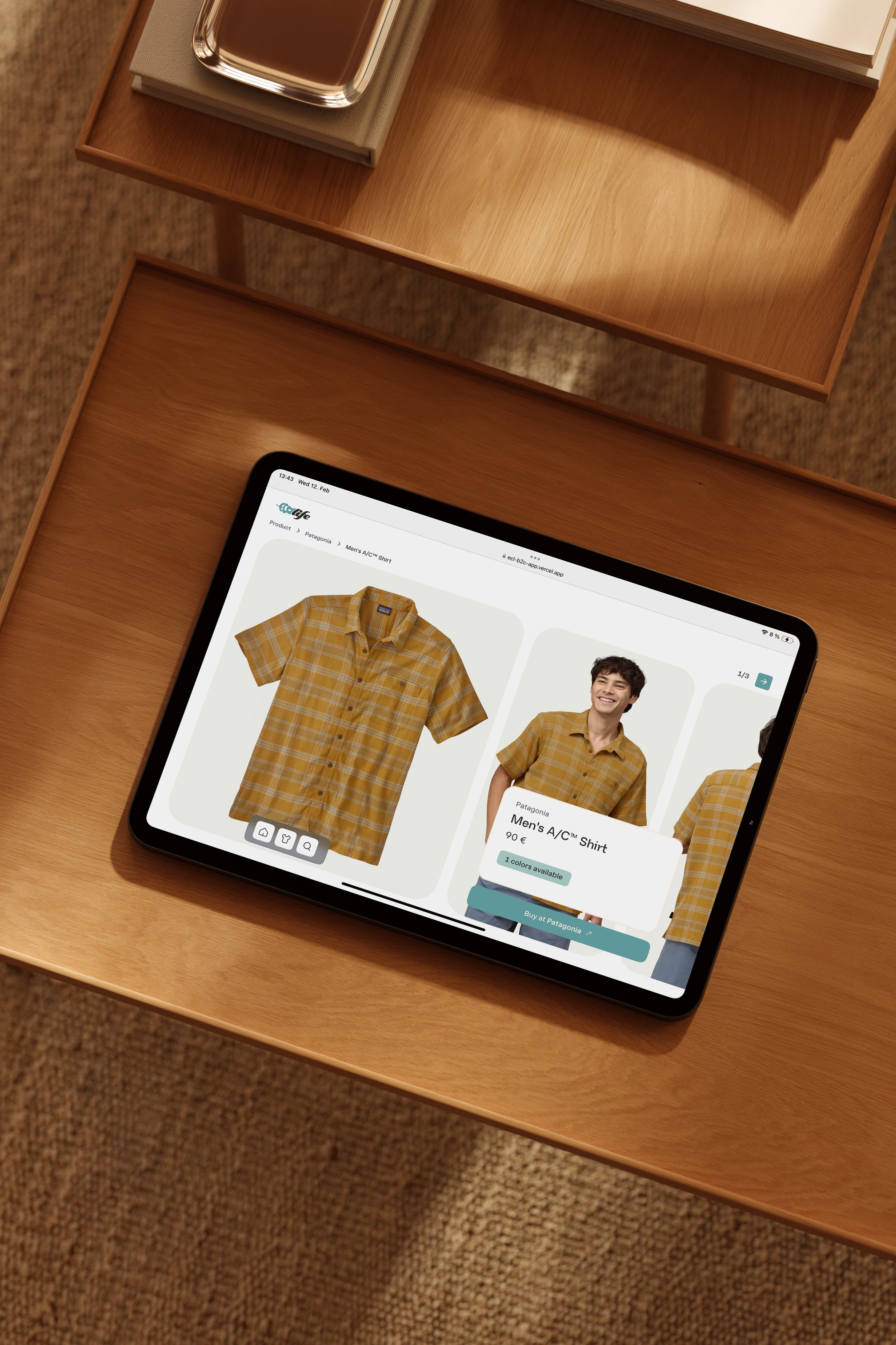 Tablet displaying an online shop with a yellow plaid men’s shirt featured. The shirt is described as an A/C™ Shirt. It shows options for adding to wish list and cart. The tablet is on a wooden surface with a textured background.